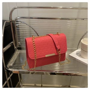 Detailed view of coral pink crossbody bag with woven texture and gold chain strap