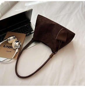 Detail of dark brown suede hobo bag placed with a laptop and headphones on white sheets