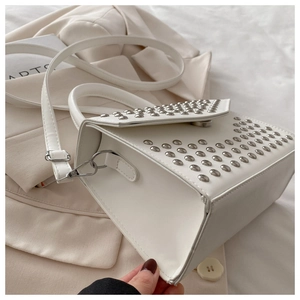 Detail of white studded handbag with silver rivets on beige blazer background