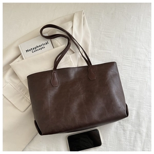 Flat lay di borsa tote marrone scuro con blazer beige e libro in scena da ufficio