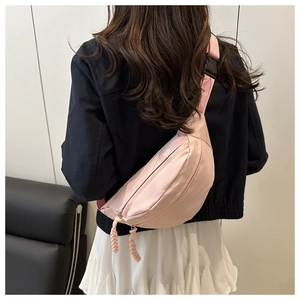 Detail of a pink nylon crescent waist bag worn across the back over a black jacket