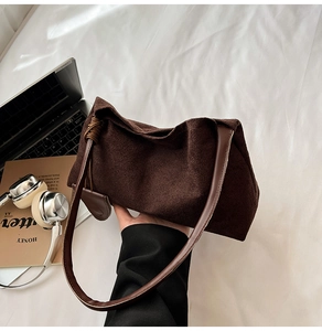 Detail of soft brown suede shoulder bag with knotted leather handle on a white fabric base