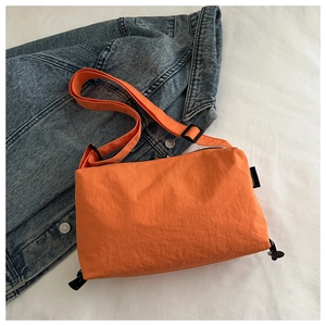 Detail of orange nylon crossbody bag featuring black zippers and adjustable strap on denim
