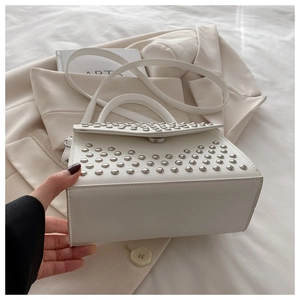 Detail of white leather handbag featuring silver studs and elegant top handle texture