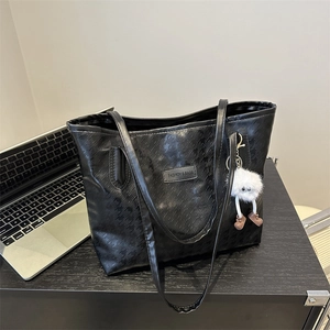 Large black star-embossed tote bag with plush charm and laptop on a dark desk