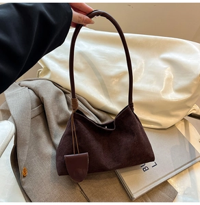 Detail of dark brown suede shoulder bag with thin straps and shield-shaped pendant tag