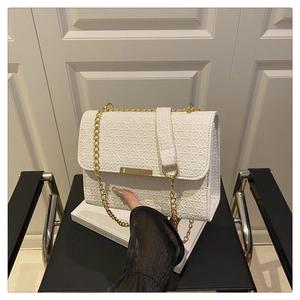 Detailed view of white woven texture crossbody bag with gold chain strap held by hand