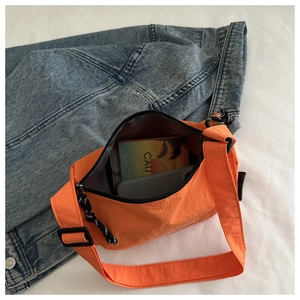Sac bandoulière en toile orange posé sur une veste en jean avec détails de la fermeture