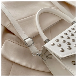 Detailed close-up of white leather handbag featuring silver studs and metal hardware