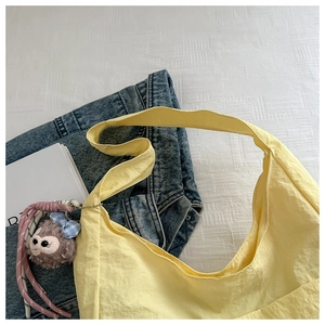 Detail of light yellow nylon tote bag featuring a plush bear charm on white fabric
