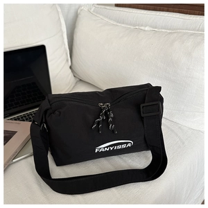 Detailed view of black nylon crossbody bag with white FANYISSA lettering on a white pillow
