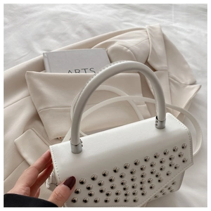 Detailed shot of white faux leather handbag with silver rivets and elegant top handle