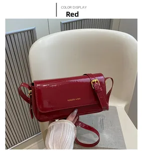 Detail of red patent leather crossbody bag with gold logo and adjustable strap