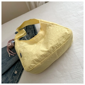 Close-up of a yellow pleated nylon hobo bag with a purple plush bunny charm on a bed