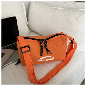 Close-up of bright orange nylon crossbody bag with logo detail and adjustable black strap