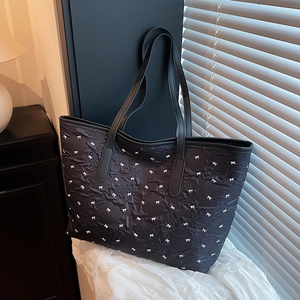 Black textured tote bag with white bow pattern and leather handles in soft lighting