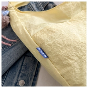 Detail of light yellow pleated tote bag featuring fashion label and plush heart charm
