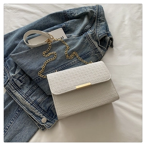Close-up of white woven leather handbag with gold metal lock and chain strap on blue denim