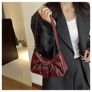 Detail of dark red patent leather shoulder bag with vintage buckles on a gray suit