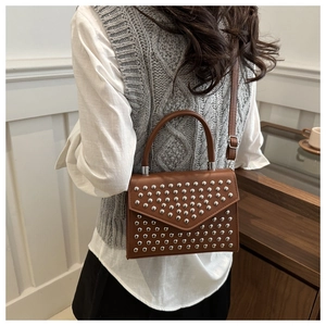 Detail of a brown leather bag featuring punk style silver studs and a fixed round handle