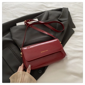Macro detail of glossy burgundy patent leather handbag with gold logo and metallic hardware