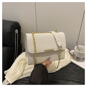 Macro shot of cream woven leather handbag with gold metal bar and elegant chain strap detail