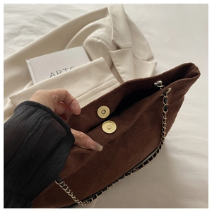 Gros plan d'un sac cabas en daim marron foncé avec fermoir magnétique doré et chaîne