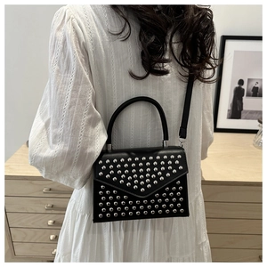 Close-up of black leather crossbody bag with silver studs on a person in cozy room
