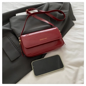 Detail of wine red patent leather shoulder bag with gold buckle on a grey suit jacket