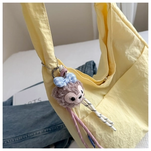 Close-up of yellow canvas tote bag featuring a cute purple plush doll pendant on strap