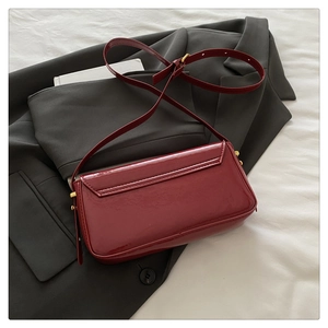 Close-up of glossy burgundy patent leather shoulder bag with gold metal hardware