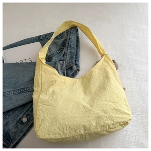 Flat lay of light yellow pleated nylon tote bag with wide shoulder strap on white texture