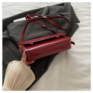 Close-up of red patent leather shoulder bag with golden buckle and textured finish