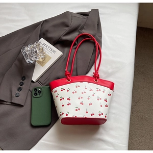 Detail of cherry print shoulder bag featuring red trim, placed on a grey blazer stylishly