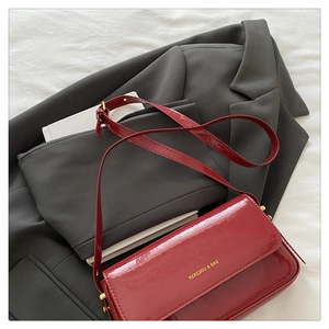 Detail of burgundy patent leather shoulder bag with gold logo on gray suit background