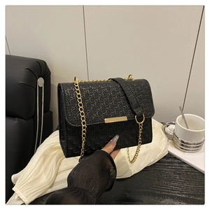 Close-up of black woven texture handbag with golden chain strap and metal hardware