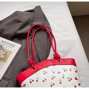 Detail of red cherry print bucket bag with knotted strap on casual blazer background
