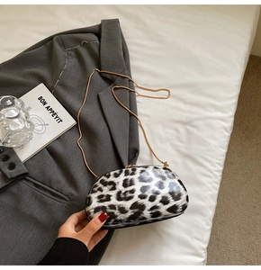 Detail of trendy leopard print shell bag with golden chain strap on a white fabric