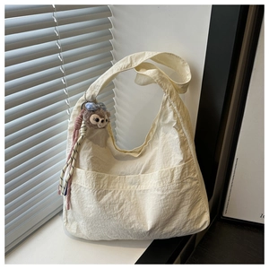 Detail of cream canvas tote with pleated texture, wide strap, and plush bear charm