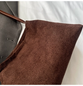 Close-up of a dark brown suede underarm bag with minimalist design and leather shoulder strap