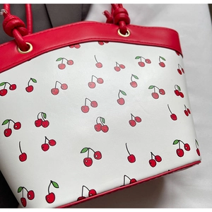 Detailed shot of cherry print handbag featuring knotted red handles and gold metal grommets