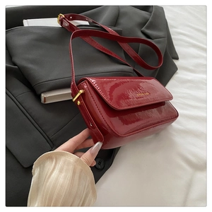 Detail of burgundy patent leather shoulder bag with gold hardware and logo branding