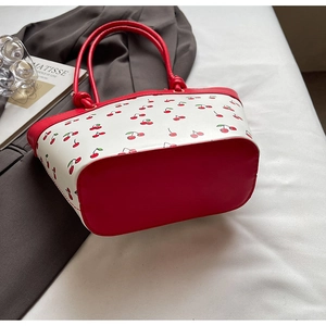 Detailed close-up of a red and white bucket bag featuring vibrant cherry prints and handles