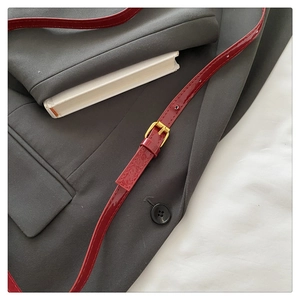 Detail of dark red patent leather strap with gold buckle on a stylish shoulder bag