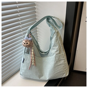 Detail of light blue nylon tote bag with texture, front pocket and plush keychain