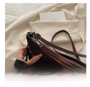 Close-up of smooth silver metal zipper and tassel detail on dark brown suede tote bag