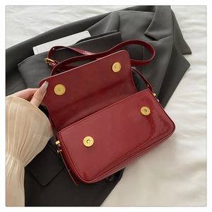 Detail of wine red patent leather shoulder bag showing glossy texture and gold magnetic snaps
