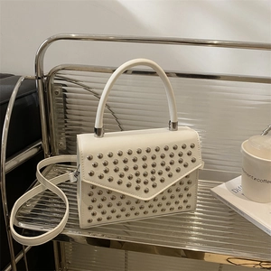 White leather handbag with silver rivets and top handle on a modern glass shelf
