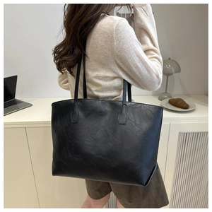 Detail of black large capacity tote bag featuring rich leather texture and shoulder straps