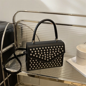 Chic black rivet handbag on a glass shelf, showing top handle and long shoulder strap